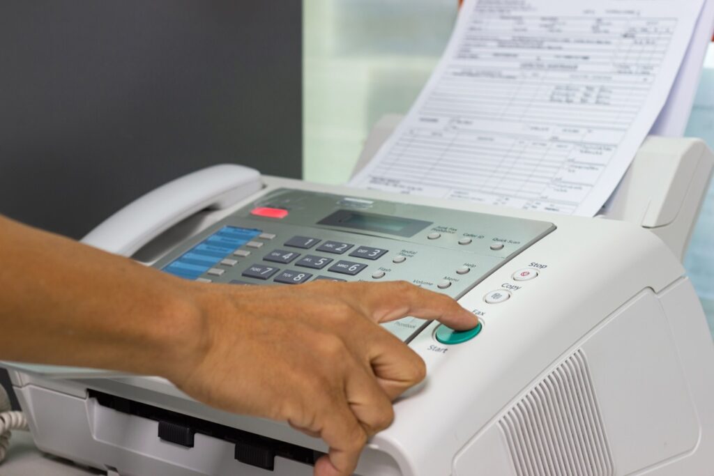 Close-up of a hand pressing the start button on a fax machine with a document being loaded for transmission