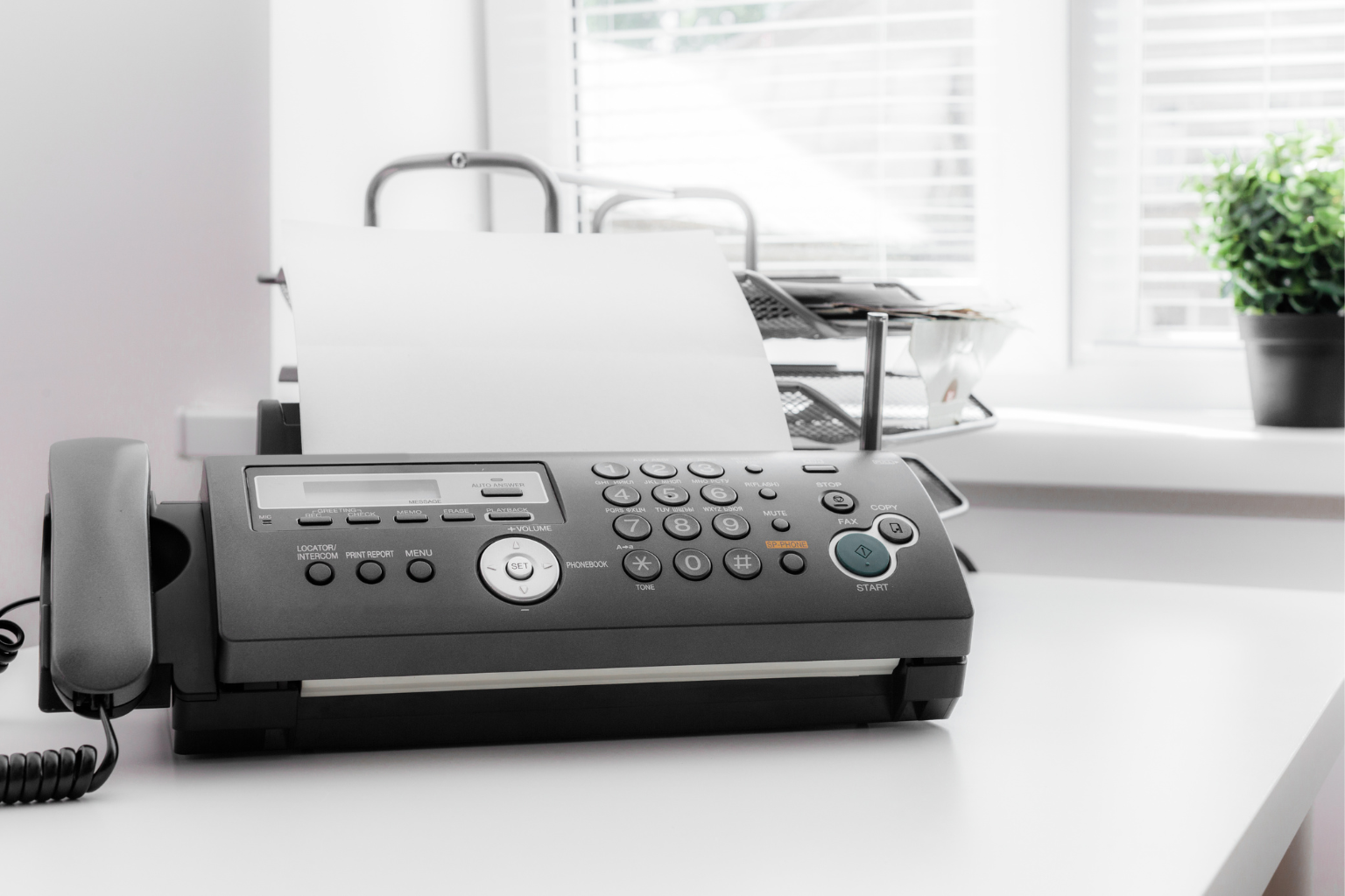 A black fax machine on a white office desk.