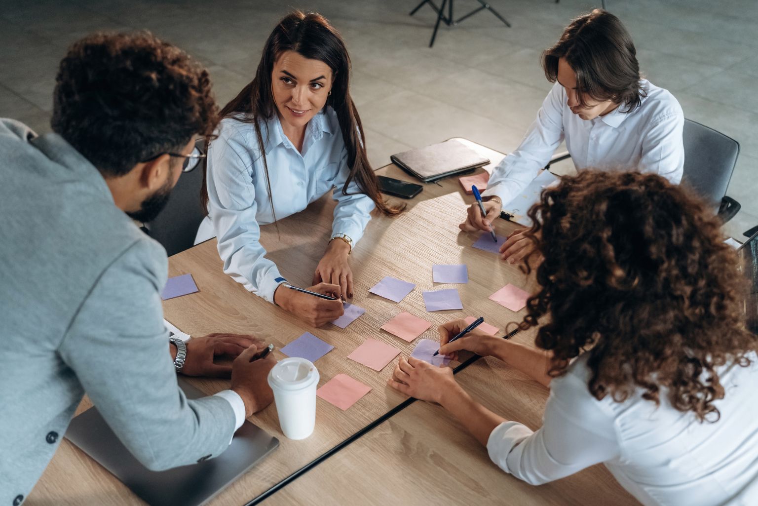 A four-member team meeting around a brown wooden table to discuss options and brainstorm ideas on sticky notes.